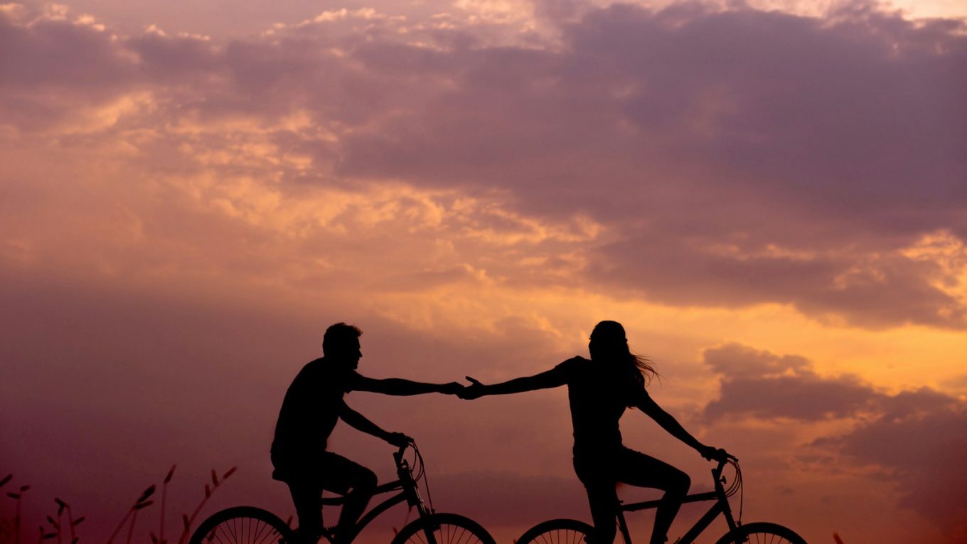 woman on bike reaching for man's hand behind her also on bike